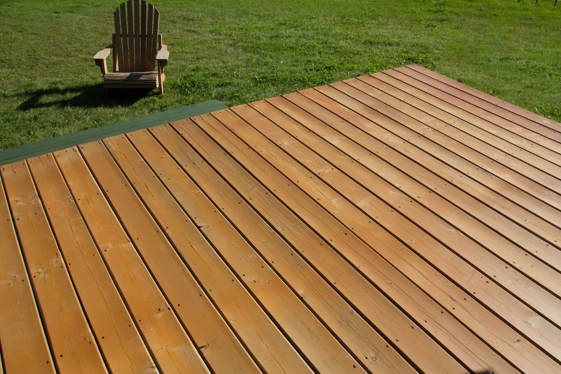 Wooden deck with diagonal planks on a grassy lawn, with a chair in the background.