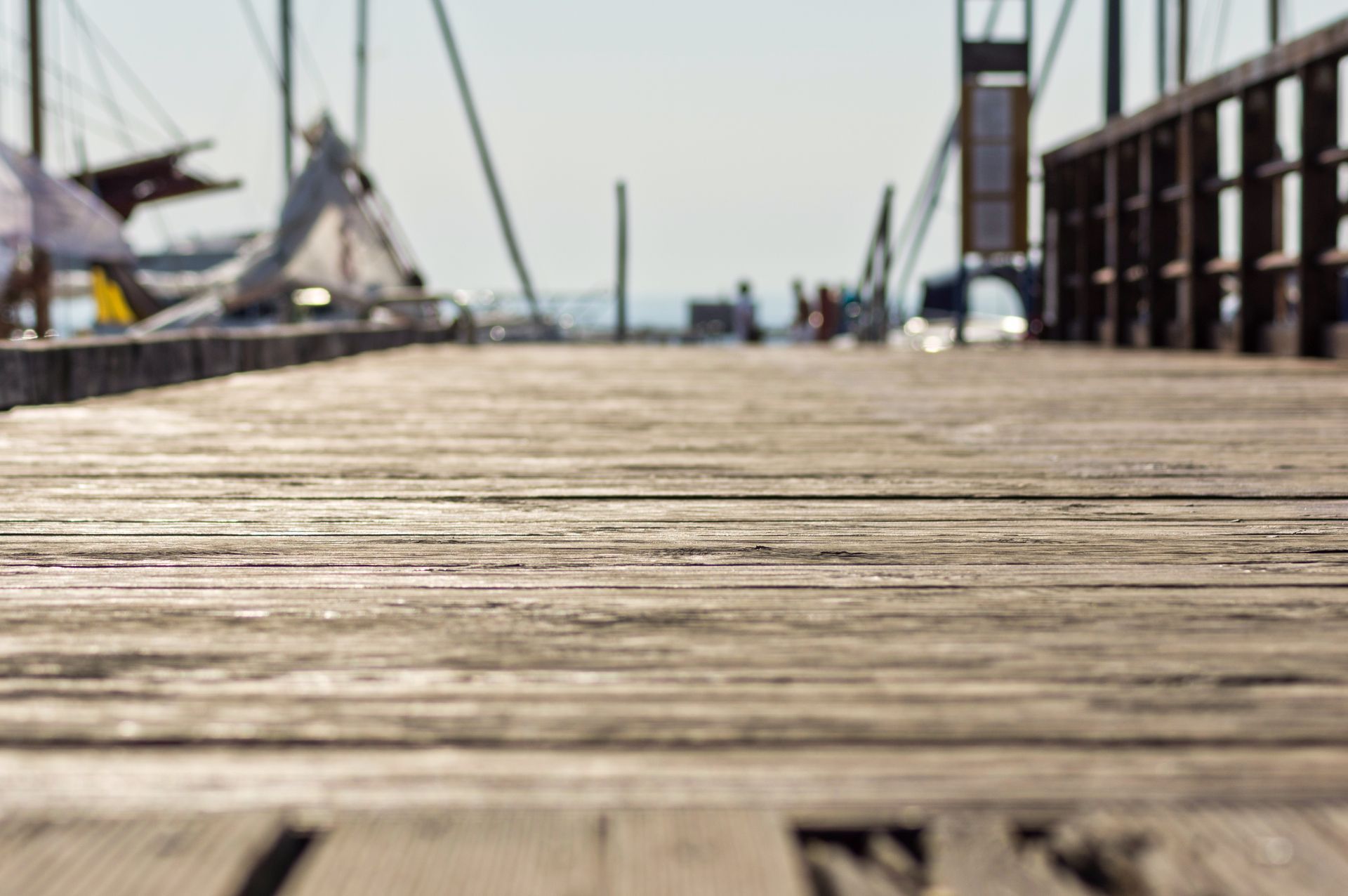 Blurred wooden boardwalk leading toward a marina with sailboats in the distance