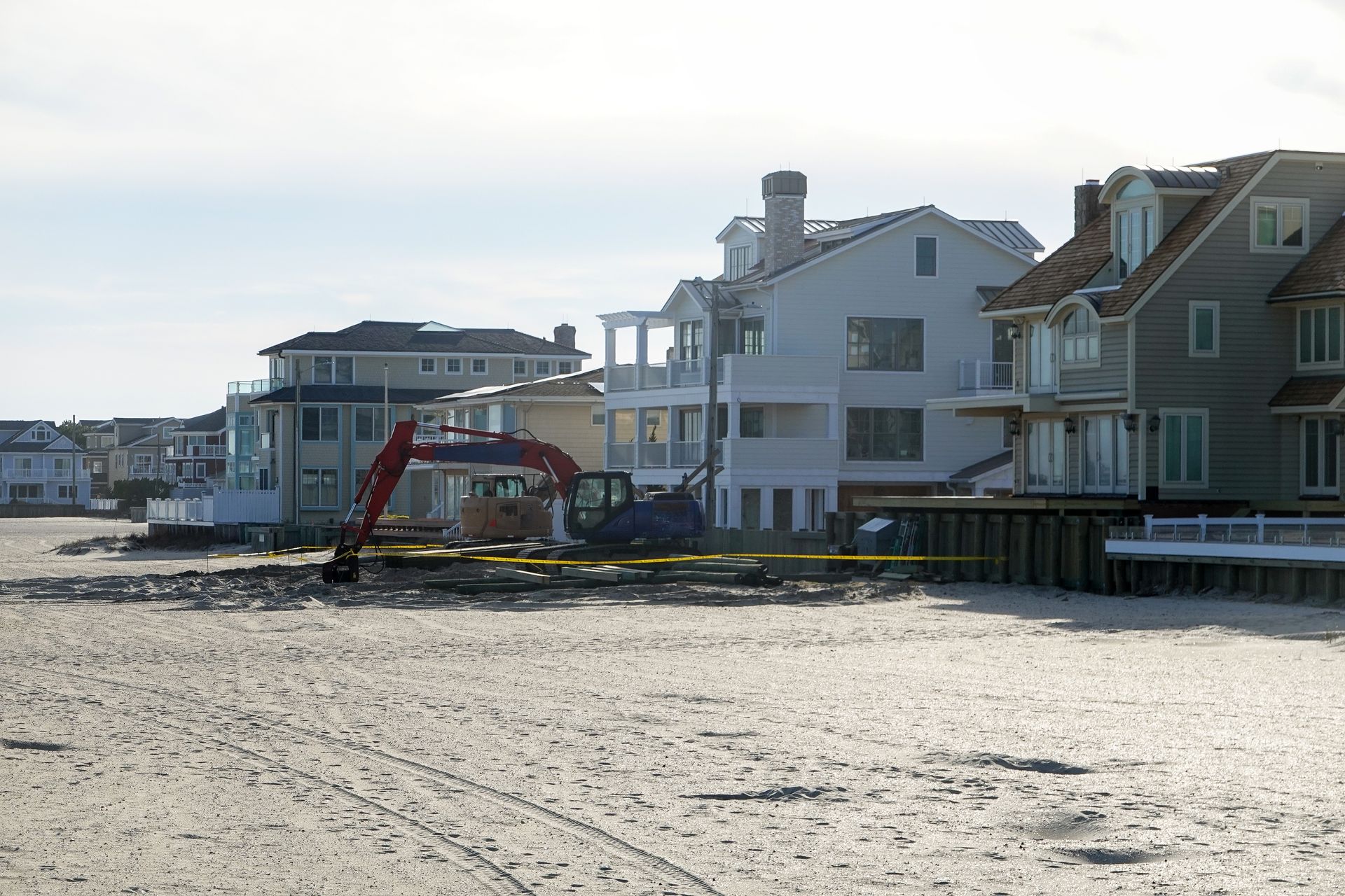 Beachfront houses with a red excavator on the sand near the shoreline