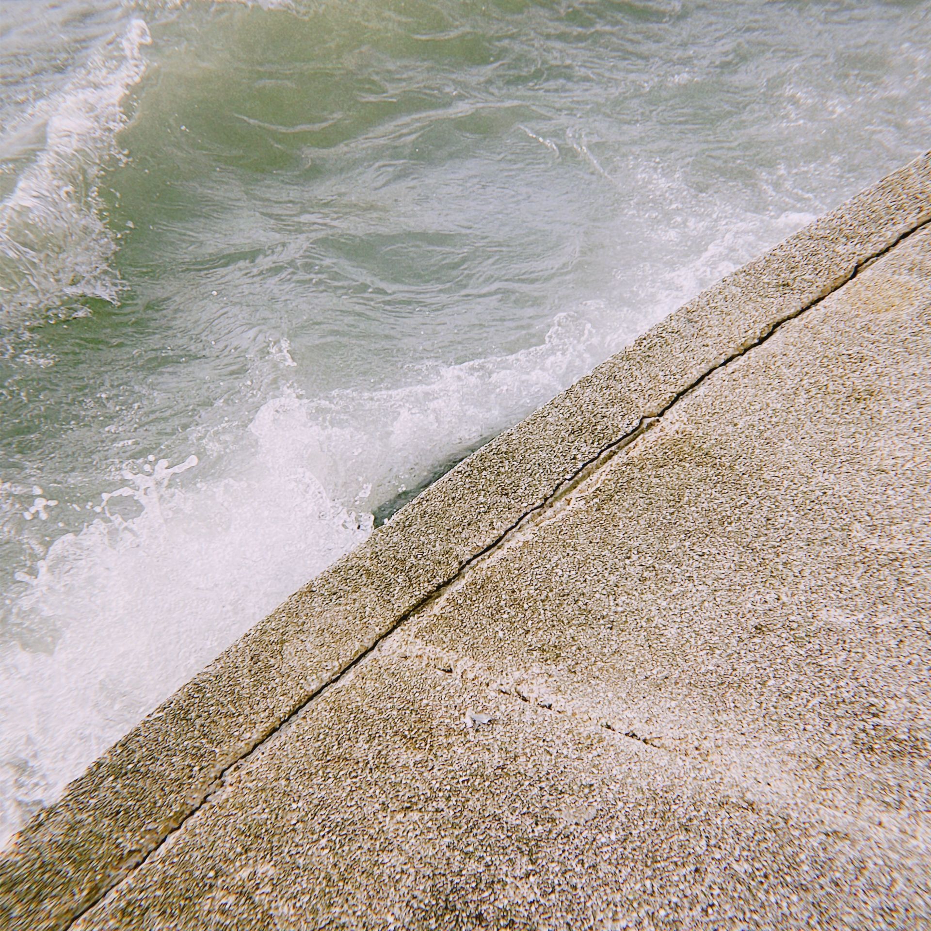 Waves washing against a sloped concrete seawall or shoreline edge