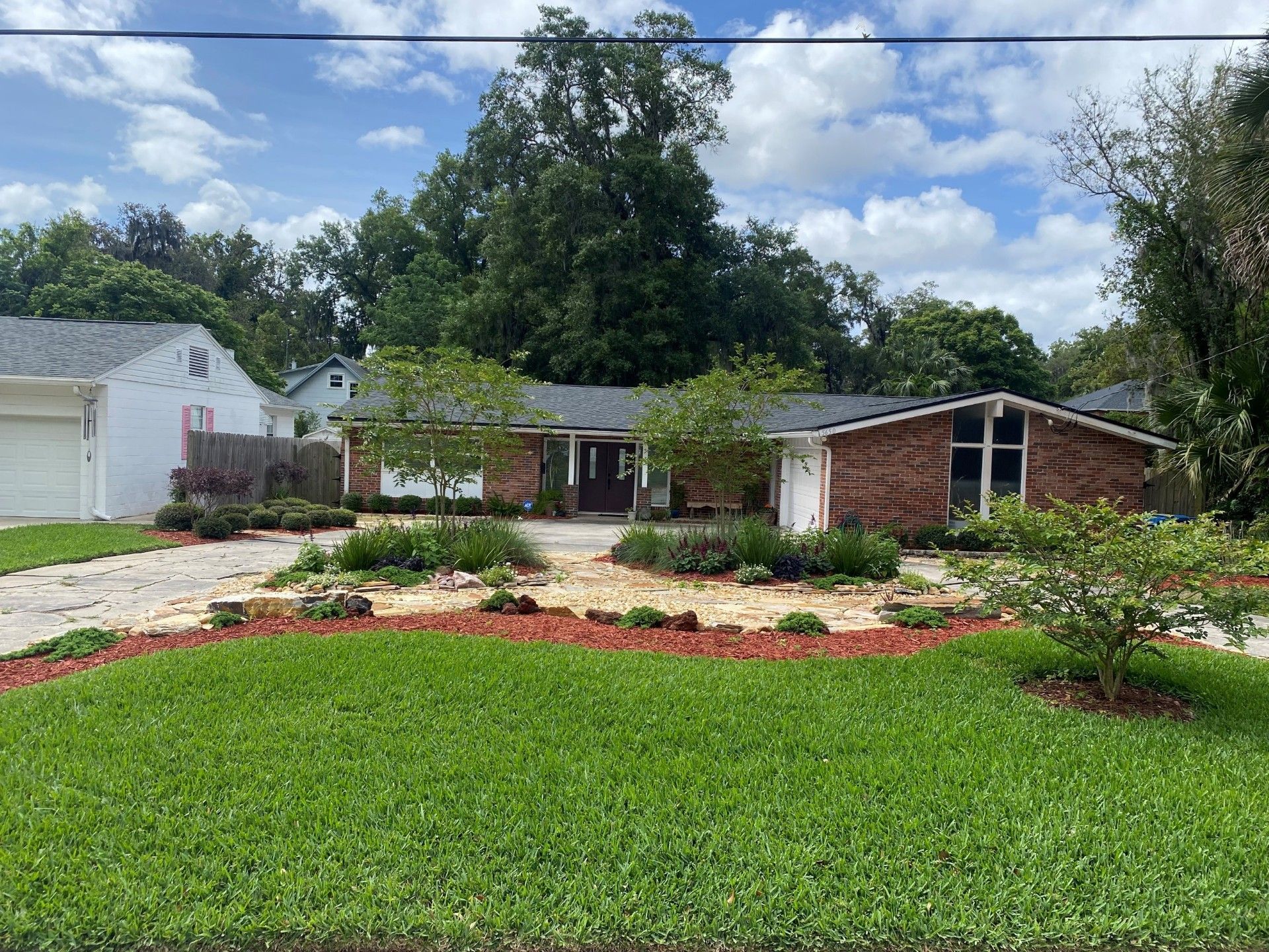 Brick house with landscaping, green lawn, trees, and blue sky with clouds.
