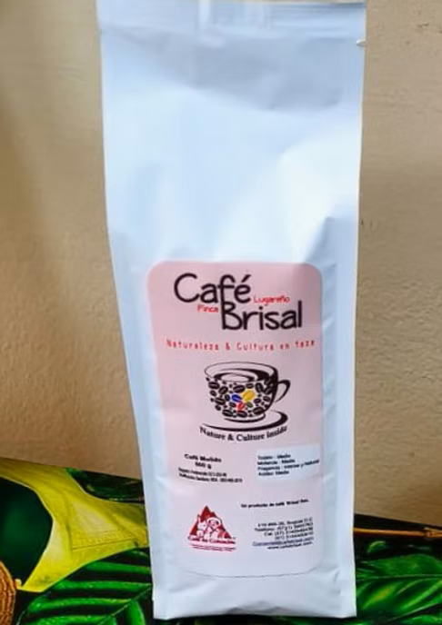 Bolsa de café White Café Brisal con logotipo y taza colorida sobre una superficie estampada verde.