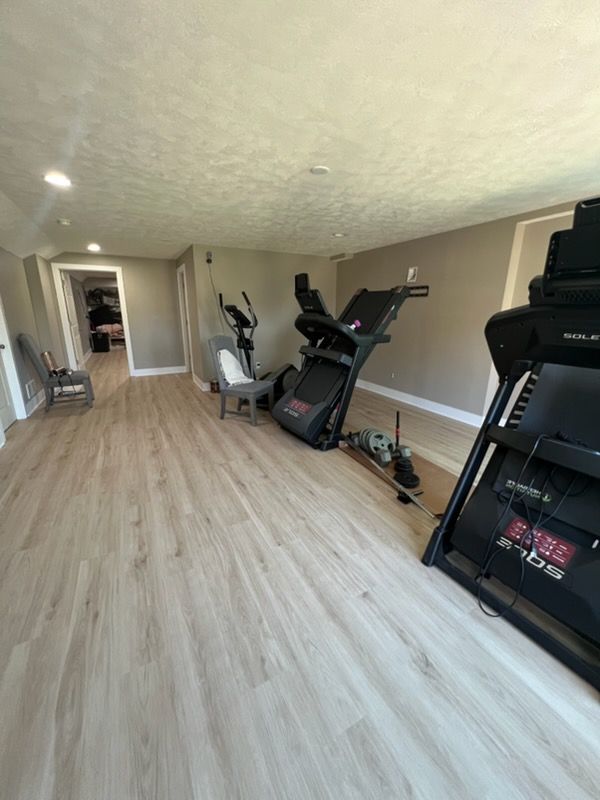Long basement room with light wood flooring, exercise equipment, and a treadmill along the wall.