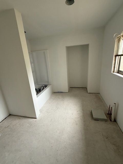 Empty unfinished room with white walls, tiled floor, a recessed alcove, and a window on the right.
