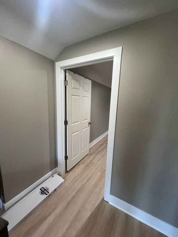 Empty hallway with gray walls, white trim, and a partially open white door on wood flooring.
