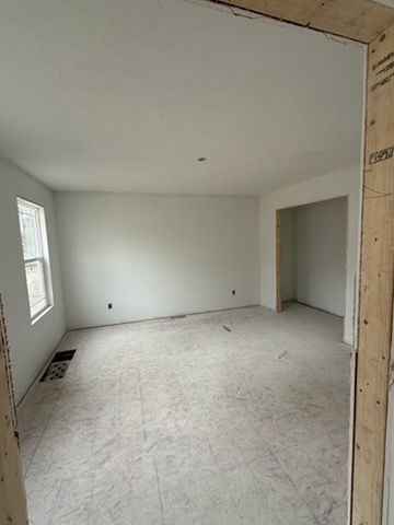 Empty unfinished room with white walls, bare floor, and a doorway opening to another space.