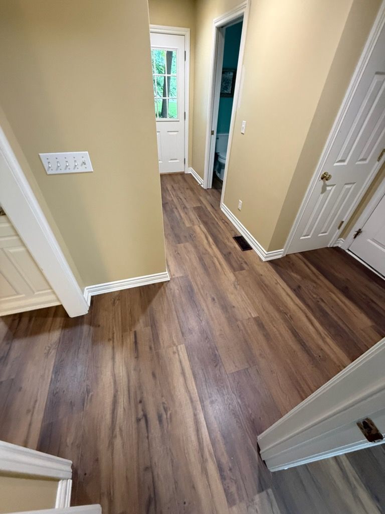 Hallway with wood flooring, beige walls, white doors, and a window at the end.
