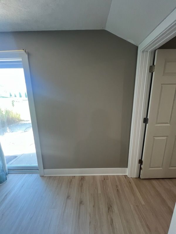 Empty room with gray walls, light wood floor, white trim, and a window by the doorway
