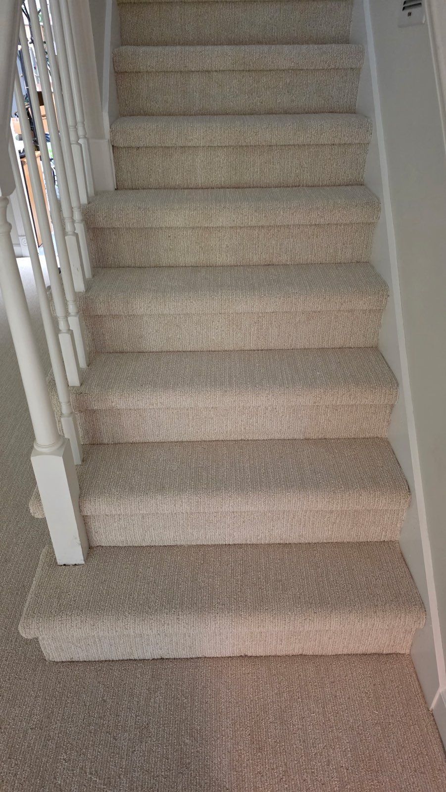 Carpeted staircase with white railings and beige walls in a narrow hallway