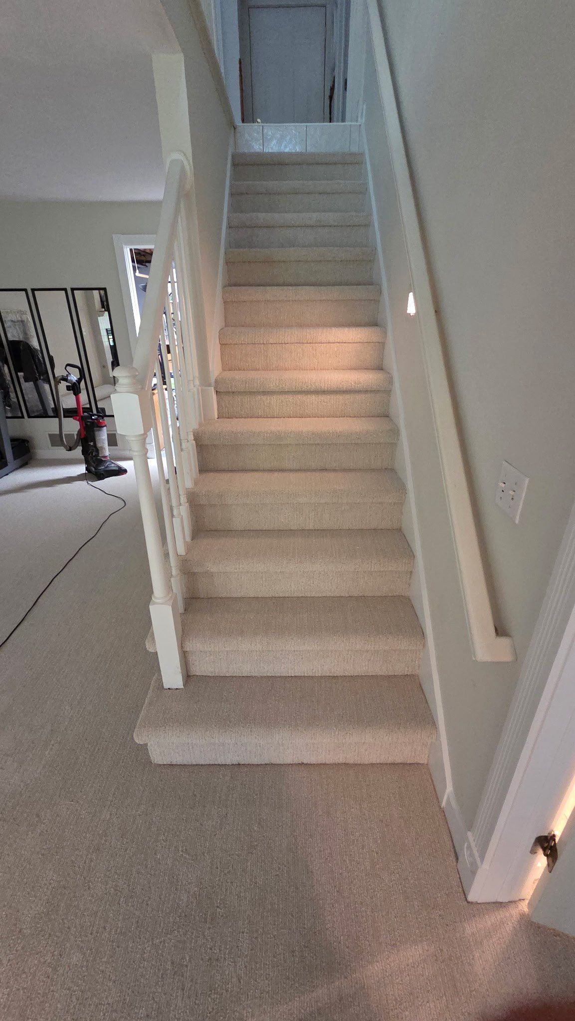 Carpeted indoor staircase with white walls and a railing, leading to an upper floor.