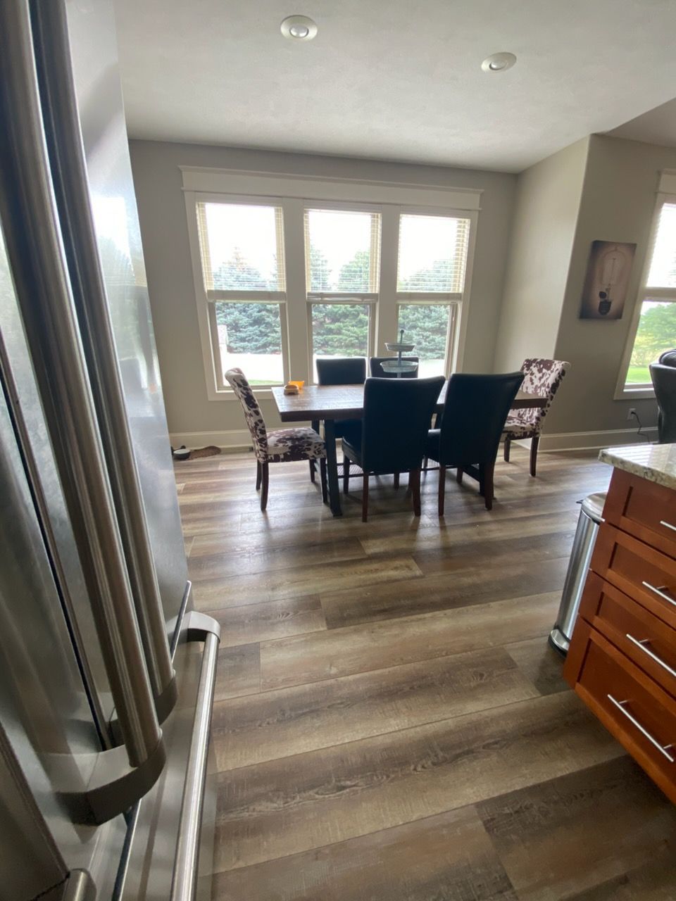 Dining room with dark chairs around a table, large windows, and wood floors in a bright home interior