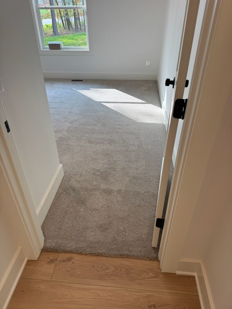Open doorway from hardwood hall into carpeted room with sunlight and window view.