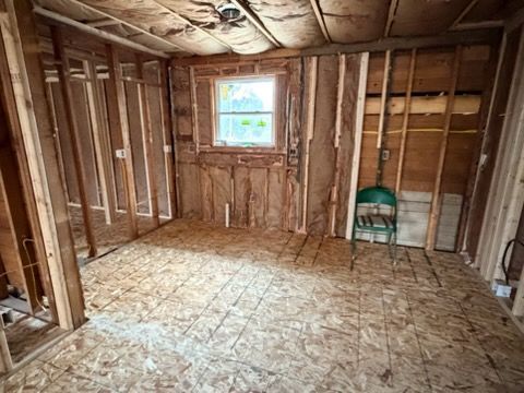 Unfinished room with exposed studs, OSB floor, and a small window; green chair near the back wall