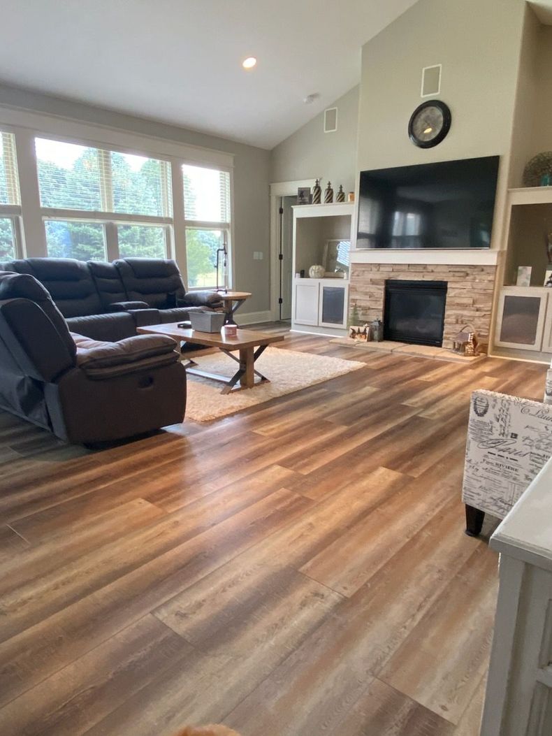 Bright living room with wood floors, dark recliner, fireplace, TV, and large windows