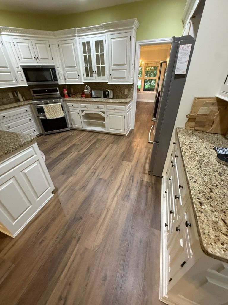 Bright kitchen with white cabinets, wood-look floor, granite counters, and an open doorway to another room