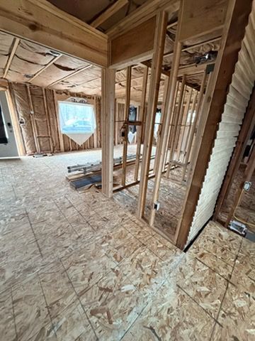 Unfinished interior with exposed wooden framing, OSB subfloor, and a window letting in daylight