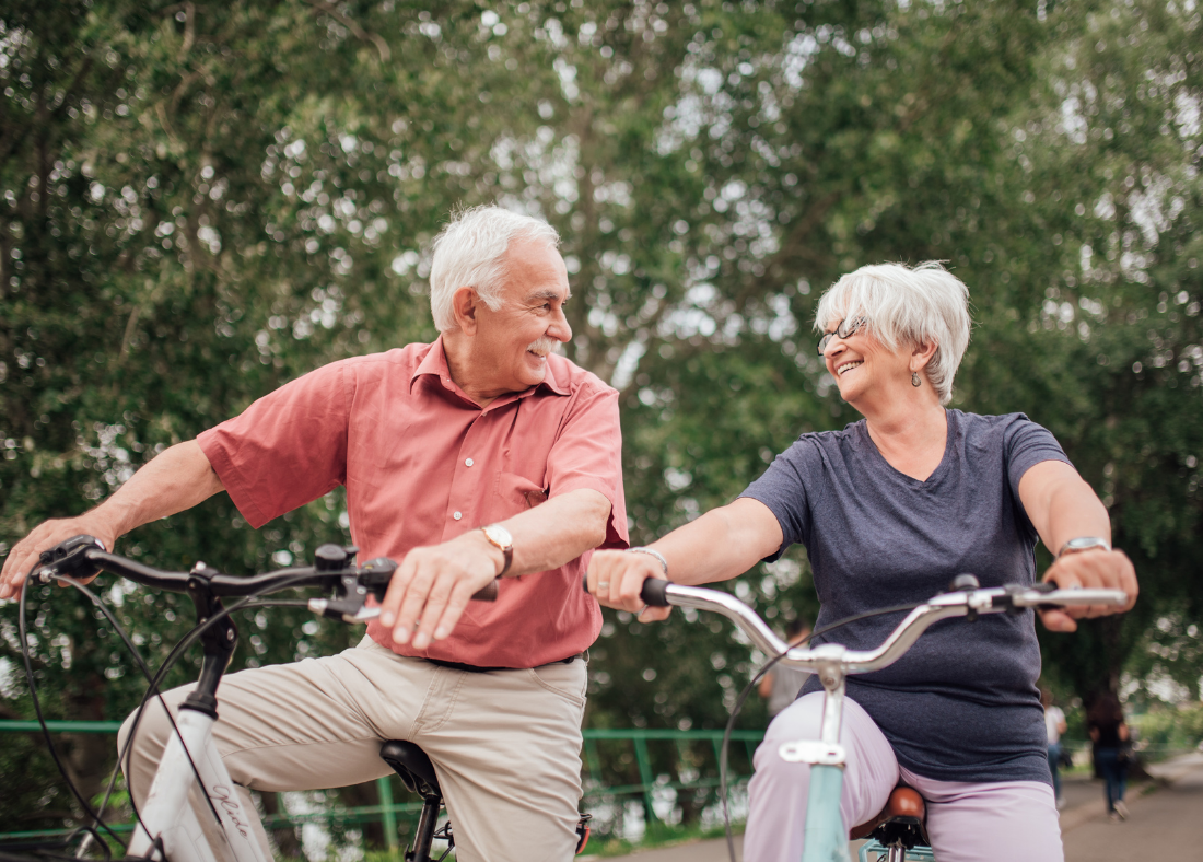 Older couple riding bikes together, laughing.