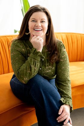Blair Drake smiling on an orange couch in a green blouse