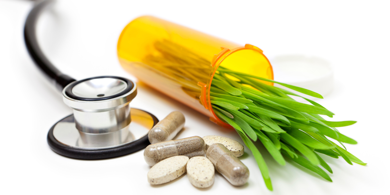 Stethoscope, green herbs, and pills beside an amber pill bottle on a white background