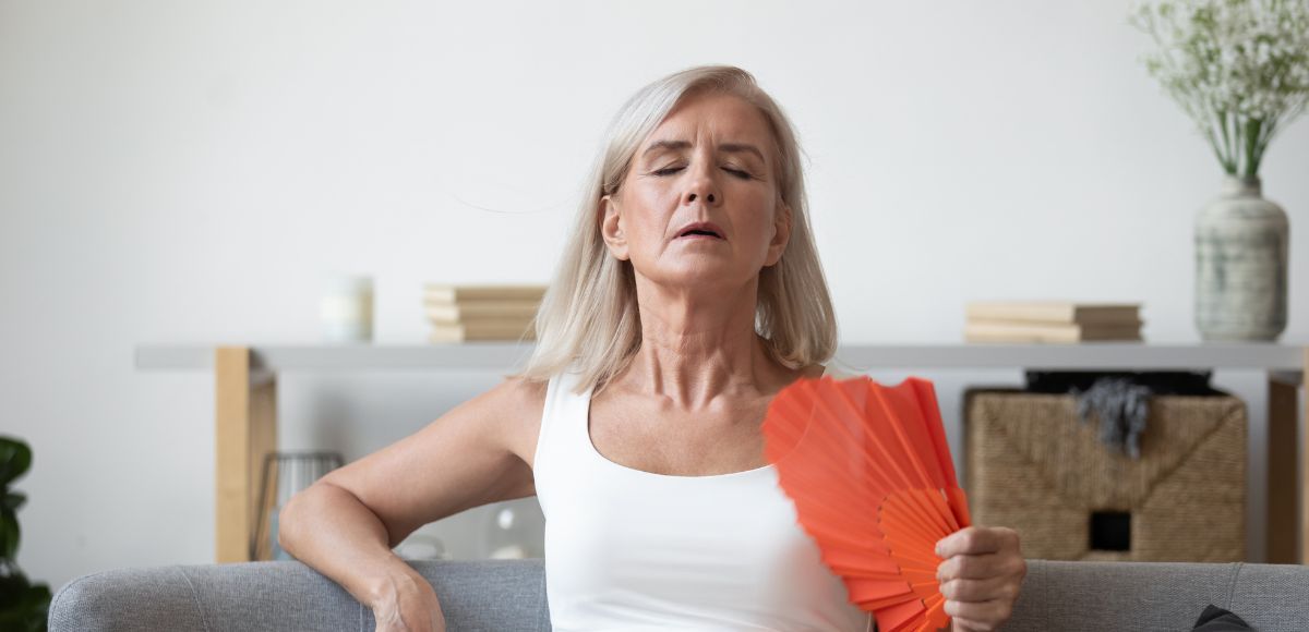 Person resting on a couch, holding a red fan and fanning themselves indoors.