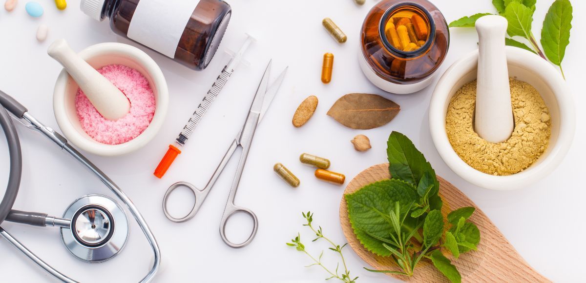 Natural wellness flat lay with mortar and pestles, herbs, pills, scissors, and a stethoscope on a white background