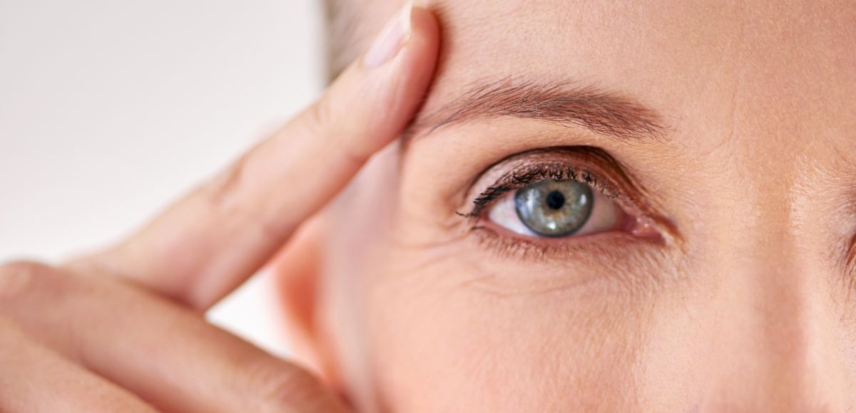 Close-up of a blue eye with fingers gently touching the temple on a light background