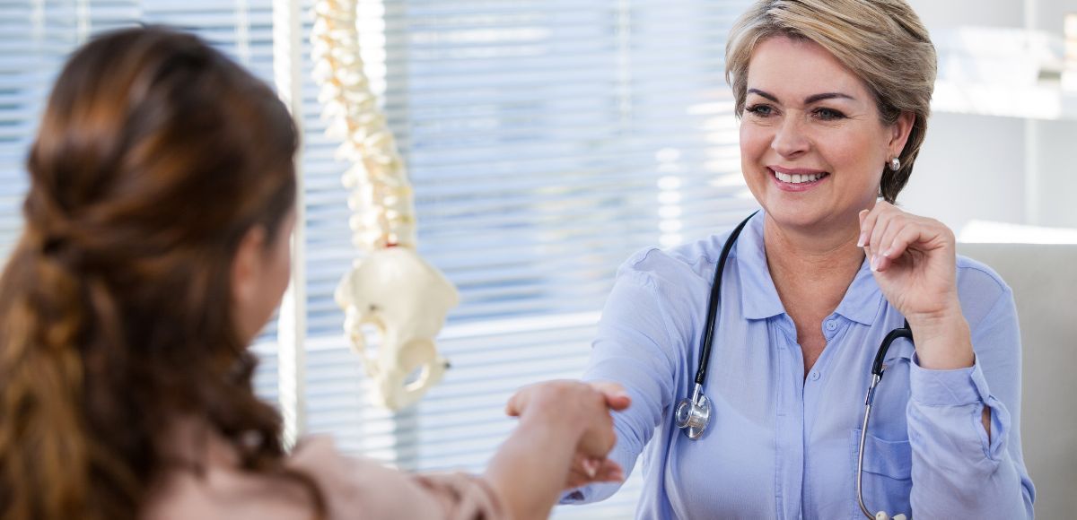 Doctor smiling and shaking hands with a patient in a bright clinic office