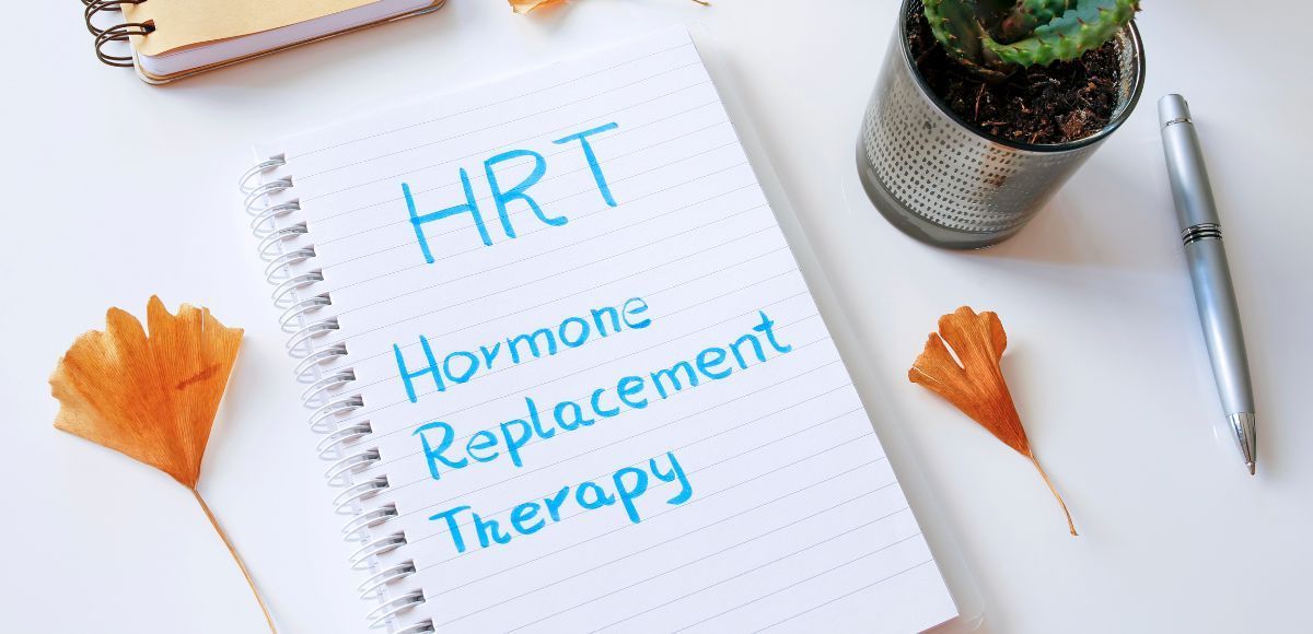Notebook with “HRT Hormone Replacement Therapy,” surrounded by autumn leaves, a pen, and a succulent plant.