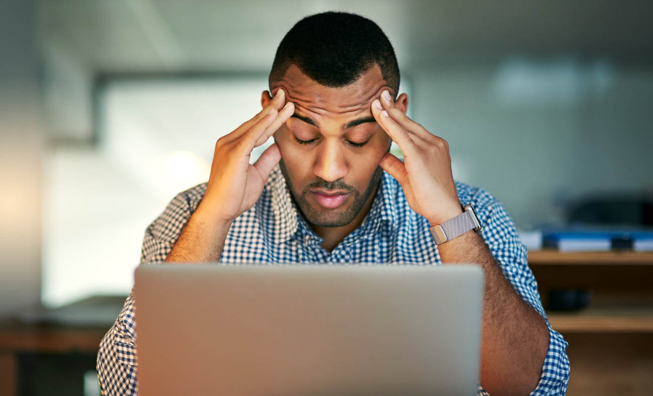 Man holding head in hands while working on laptop