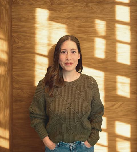 Laura Greenberg smiling indoors, wearing an olive sweater.