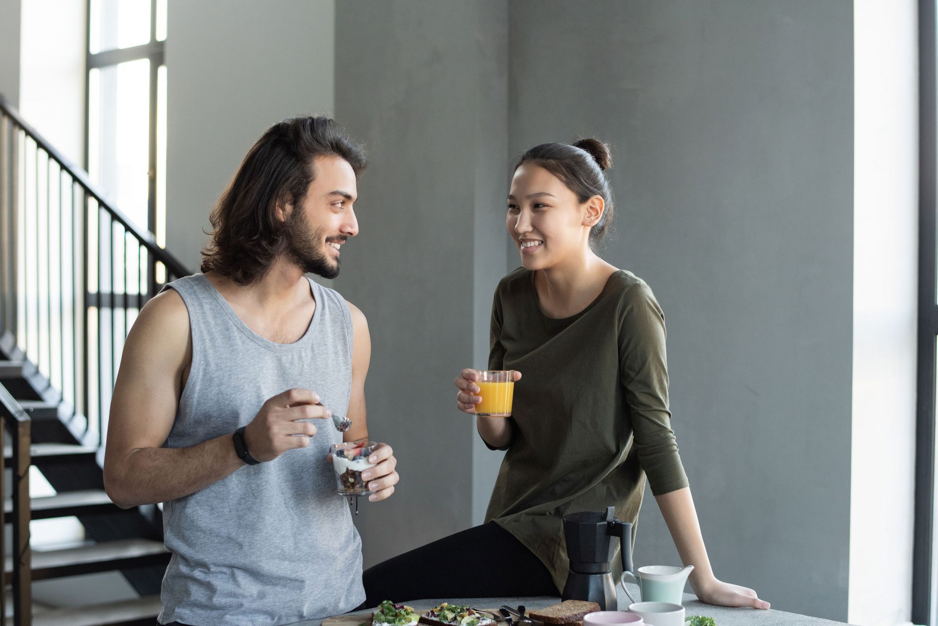 Two people chatting in a bright kitchen, holding drinks and smiling near a table.