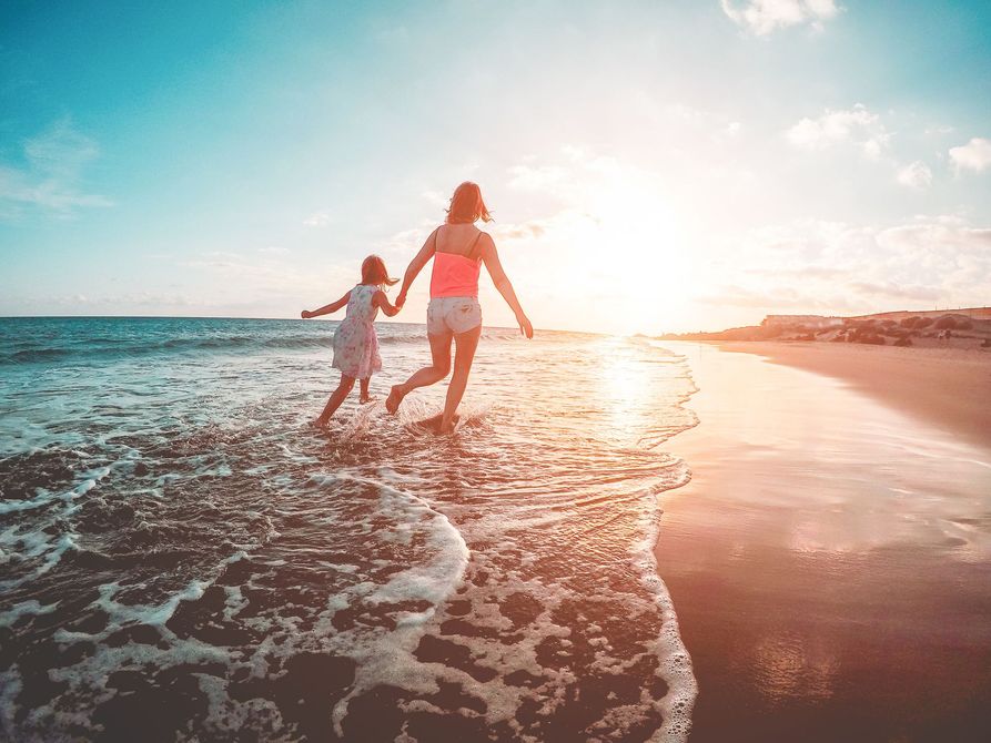 A woman and a child are running on the beach at sunset.