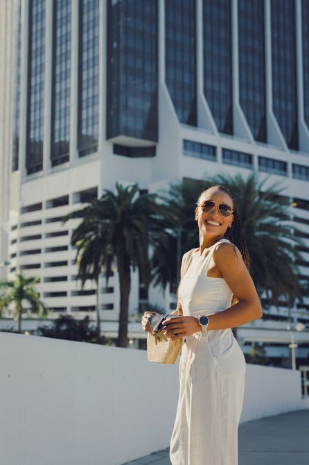 A woman in a white dress is standing in front of a tall building.