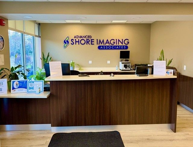 Reception desk at Advanced Shore Imaging, with wood counter, blue logo wall, and waiting area seating