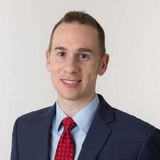 Portrait of a smiling man in a navy suit and red tie against a light background