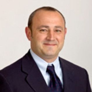 Studio portrait of a smiling man in a dark suit and tie on a white background