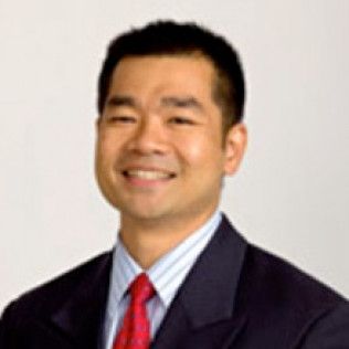 Portrait of a smiling man in a dark suit and red tie against a light background