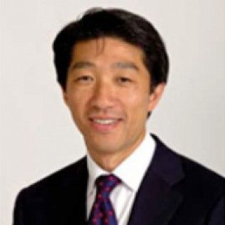 Portrait of a smiling person in a dark suit, white shirt, and purple tie against a light background