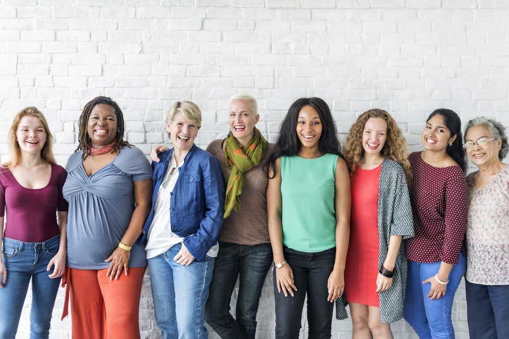 Seven people standing shoulder to shoulder against a white brick wall, smiling at the camera.