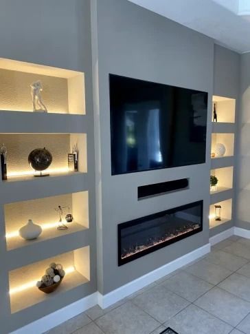 Modern living room wall with large TV, linear fireplace, and illuminated built-in shelves.