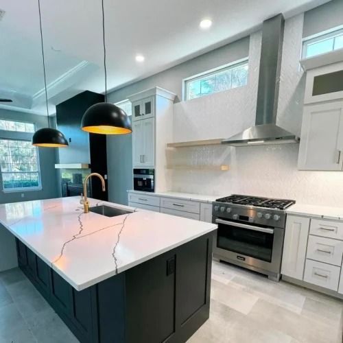Modern white kitchen with black island, pendant lights, stainless stove, and marble countertops