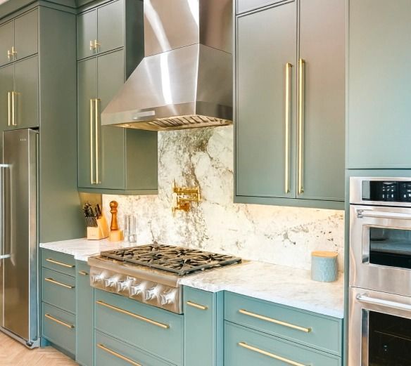 Elegant kitchen with teal cabinets, marble backsplash, stainless hood, and built-in oven.