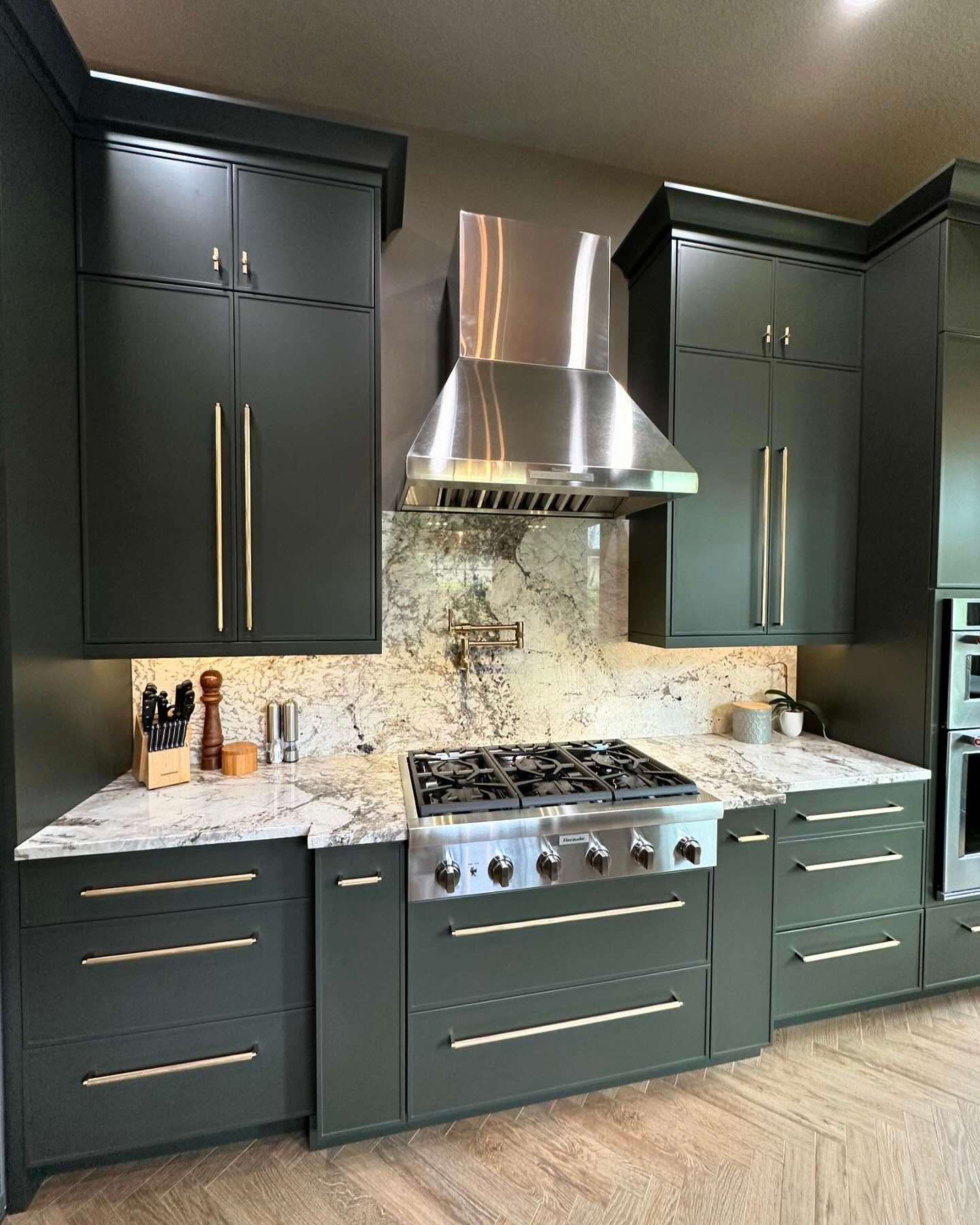 Dark modern kitchen with black cabinets, marble backsplash, stainless range, and a large hood.