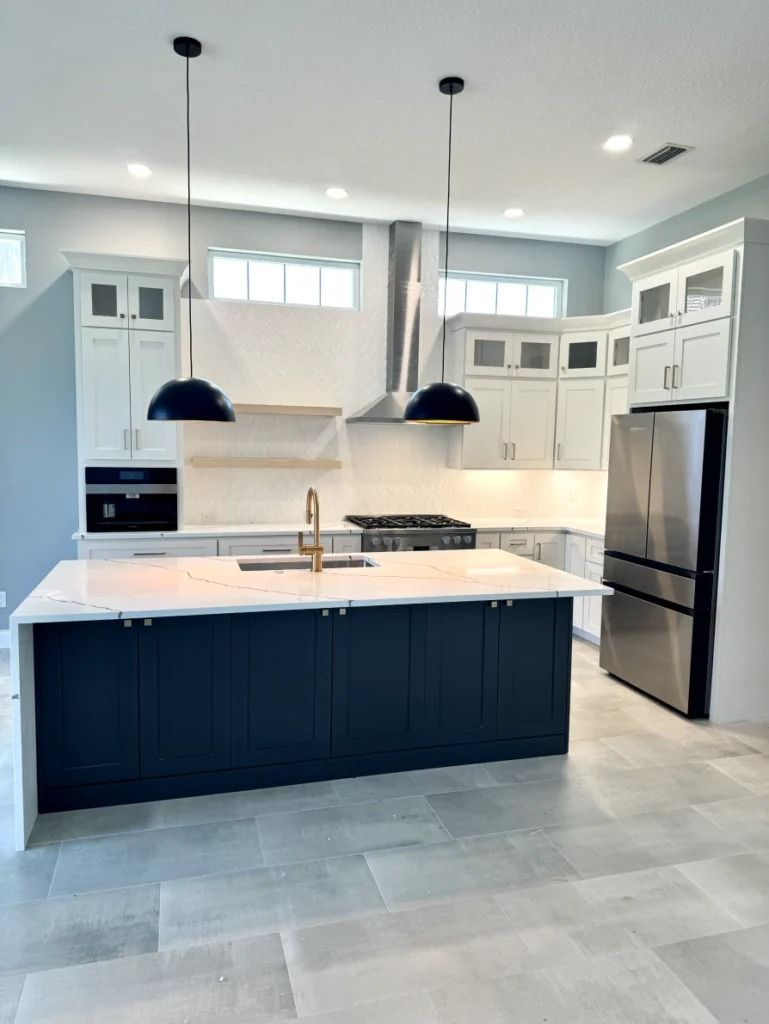 Modern kitchen with dark island, white cabinets, stainless fridge, and two pendant lights