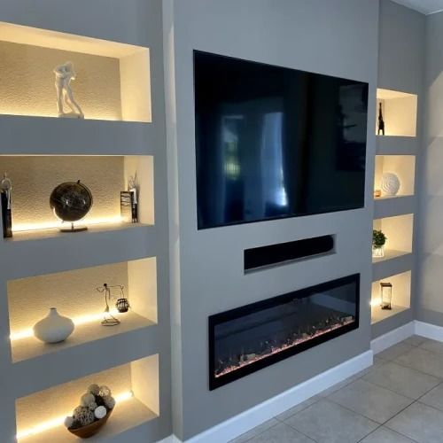 Modern living room wall with mounted TV, electric fireplace, and illuminated built-in shelves displaying decor