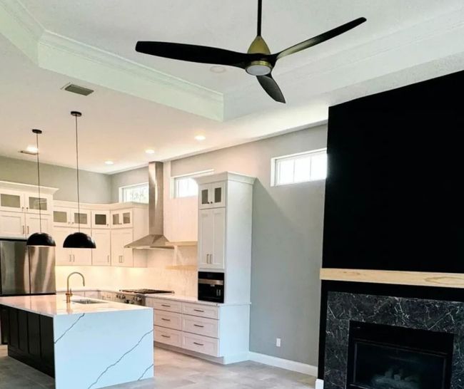 Modern white kitchen and living area with island, black pendant lights, ceiling fan, and fireplace accent wall