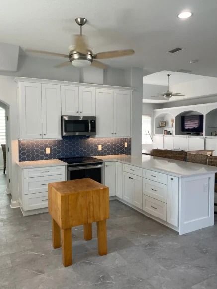 Bright modern kitchen with white cabinets, stainless appliances, gray tile floor, and a wooden island stool