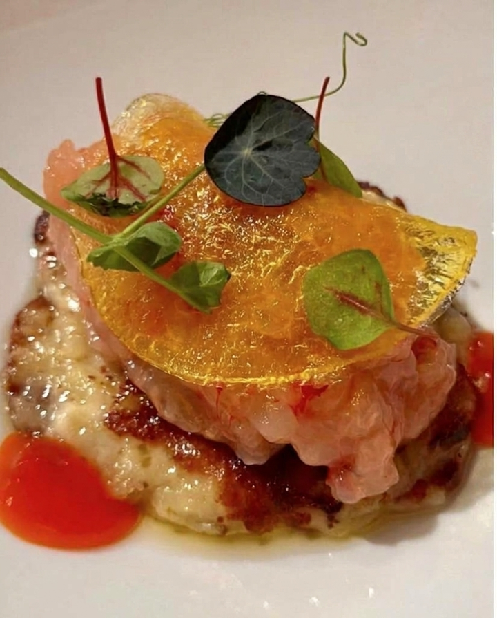 Piatto gourmet impiattato con cialda all’arancia, erbe verdi e salsa rossa su un piatto bianco