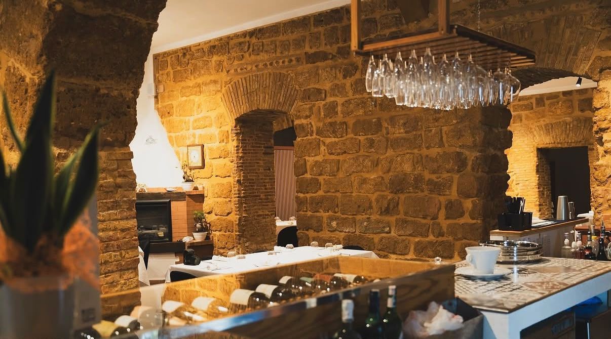 Calda sala da ristorante con pareti in pietra, tovaglie bianche e un lampadario di cristallo sopra un buffet.