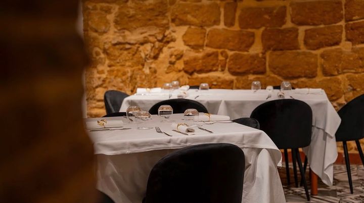 Tavoli vuoti con tovaglie bianche in una sala da pranzo dalle pareti di pietra, poco illuminata